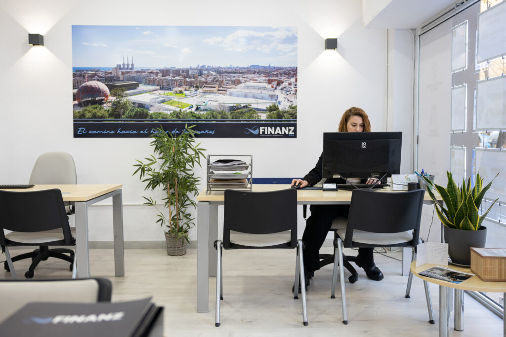 Oficina de Finanz en Badalona con trabajadora en su escritorio y mural panorámico de la ciudad al fondo.